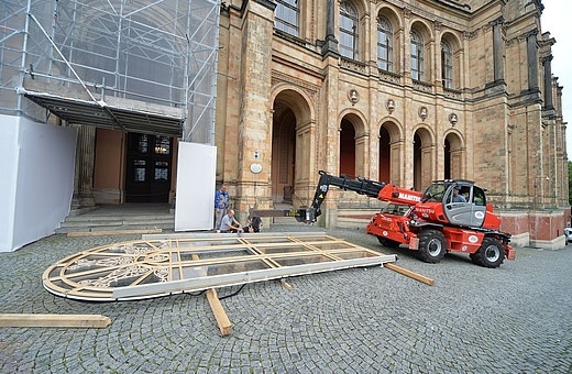 Roter Manitou-Teleskoplader hebt ein großes Holzelement vor einem historischen Gebäude