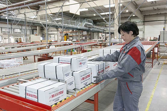 Mitarbeiterin sortiert Manitou-Ersatzteilkartons auf einem Rollband