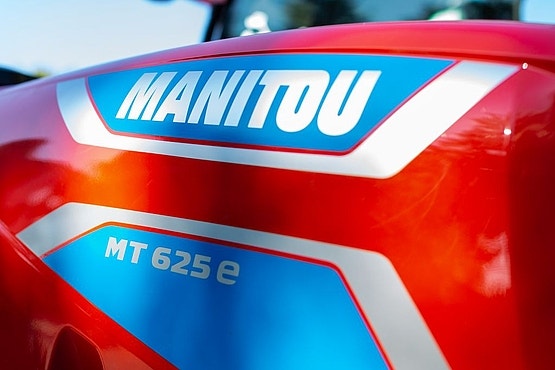 Nahaufnahme der roten Motorhaube eines Manitou MT 625 e mit blau-weißem Markenlogo