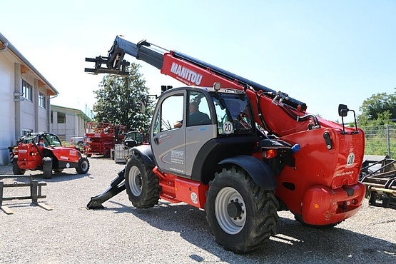 Roter Manitou-Teleskoplader mit ausgefahrenem Ausleger steht auf einem Hofgelände vor einem Gebäude