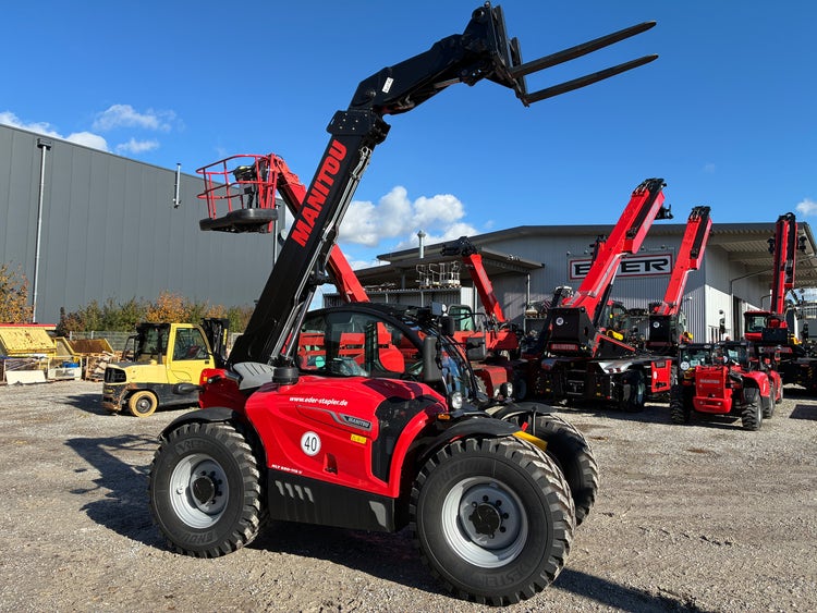 Manitou MLT 630-115 D von der linken Seite mit angehobenen Gabeln auf dem Hof bei EDER Stapler.