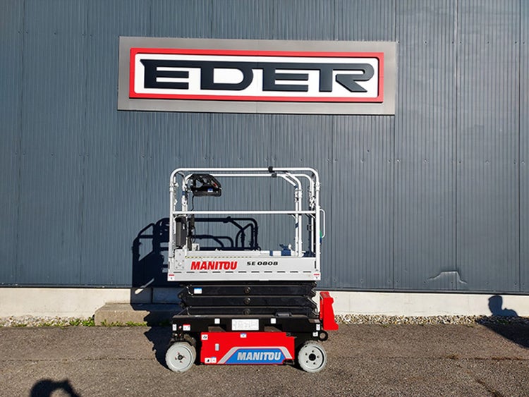 Manitou SE 0808 Scherenarbeitsbühne in eingefahrener Position vor einem Industriegebäude mit EDER-Logo bei Tageslicht.