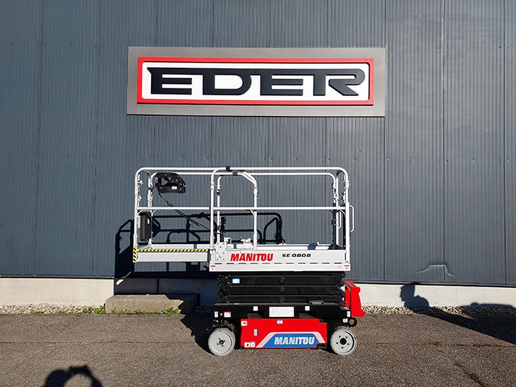 Manitou SE 0808 Scherenarbeitsbühne in eingefahrener Position, stehend vor einem Industriegebäude mit EDER-Schriftzug.