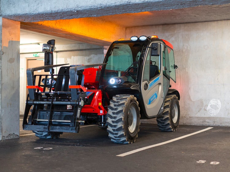Kompakter Teleskoplader in einem Parkhaus, geparkt in einer markierten Parklücke mit niedriger Deckenhöhe.