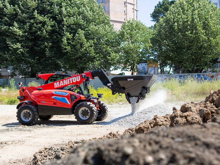 Roter Teleskoplader der Marke Manitou auf einer Baustelle beim Entladen von Kies aus einer Schaufel.