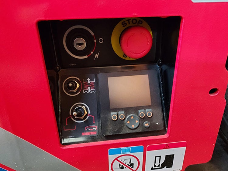 Detailansicht des Steuerpanels an der Basis der Manitou SE 0808 Scherenarbeitsbühne mit Not-Aus-Schalter und Display.