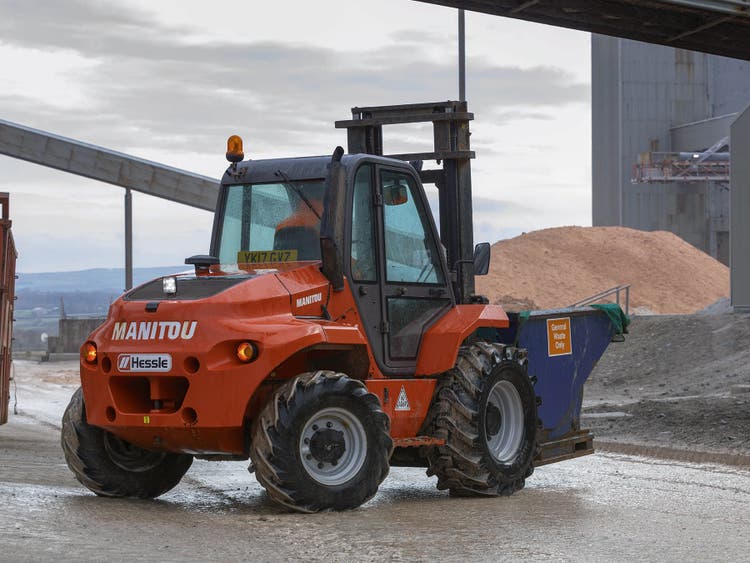 Roter Manitou-Geländestapler auf einem Industriegelände, beladen mit einem Container