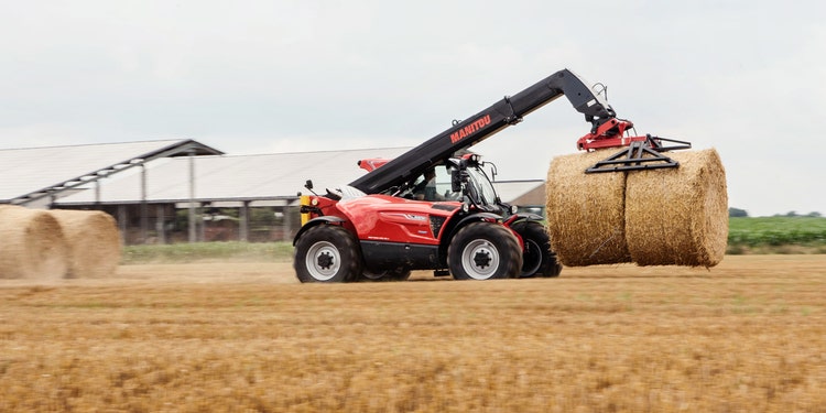 Roter Manitou-Teleskoplader hebt eine große Rundballen-Strohrolle auf einem Feld