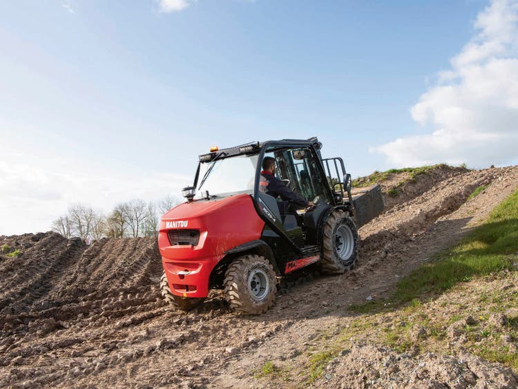 Roter Manitou-Geländestapler fährt eine unebene, schlammigen Hügel hinauf
