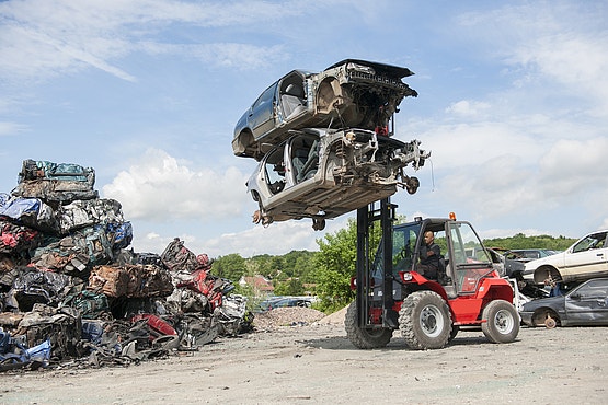 Roter Manitou-Geländestapler hebt zwei ausgeschlachtete Autowracks auf einem Schrottplatz