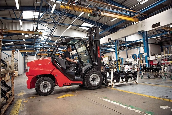 Roter Manitou-Gabelstapler im Einsatz in einer Industriehalle, zwischen Maschinen und Produktionsanlagen.