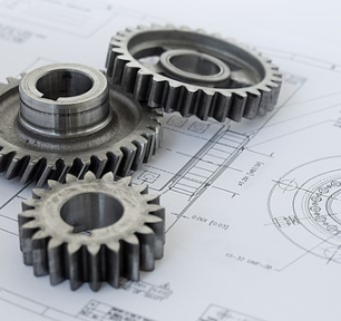 Mehrere Metallzahnräder liegen auf technischen Konstruktionszeichnungen