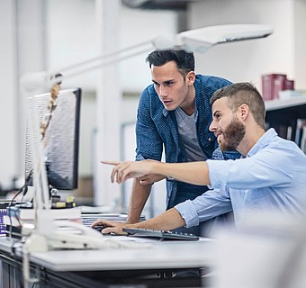 Zwei Männer arbeiten gemeinsam am Computer in einem modernen Büro und besprechen etwas auf dem Bildschirm