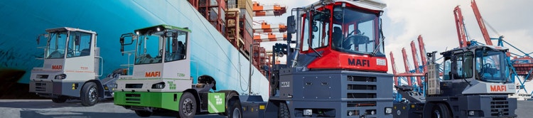 Vier MAFI-Terminalzugmaschinen in unterschiedlichen Modellen stehen vor einem Frachtschiff