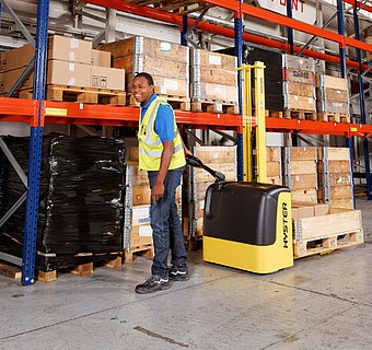 Bild von einem Mann der mit einem Hochhubwagen durch ein Lager geht