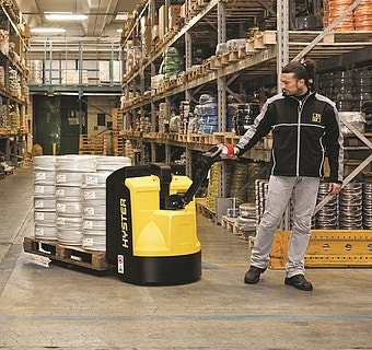 Bild von einem Mann der mit einem Hand- und Niederhubwagen durch ein Lager geht